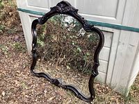 Full view of the framed mirror resting outdoors showing the overall shape and style.