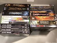 Stack of Xbox 360 and PC game cases including Star Wars games, Guitar Hero, Diablo III, and others, plus Memorex OptiFix Pro system.