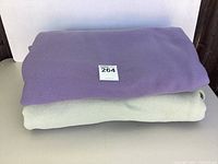 Two folded Polartec fleece blankets stacked, purple on top of gray, on a white background.