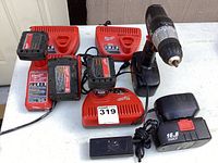 Photo showing Milwaukee cordless drill, four battery chargers, and two rechargeable batteries on white table surface