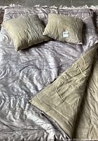 Twin reversible comforter laid flat with two matching beige textured throw pillows on top, showing front side and partially flipped reverse side
