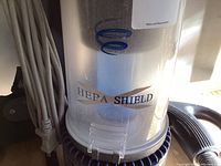 Close-up image of the HEPA Shield filtration dust canister attached to the vacuum, showing clear canister with blue spiral filter.