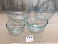 Set of four Pyrex sculpted pattern clear glass mixing bowls of different sizes arranged in a cluster on a flat surface