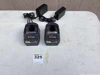 Full view of two black Ryobi 18V lithium battery chargers with attached power cords on a white surface.