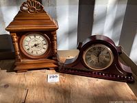 Two battery operated wooden mantel clocks placed on a wooden surface with clear visibility of design and clocks faces.