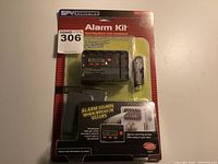 Front of sealed blister pack showing alarm device, key card, and packaging details