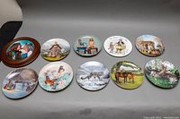 Photo showing nine 8.5 inch collectible plates arranged in a row with diverse detailed artwork