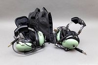 Front view of both vintage David Clark aviation headsets with green ear cups, black headbands, attached microphone arms, and the black carrying case behind them.