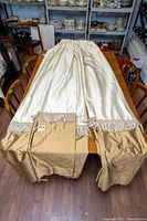 Curtain panels laid out on table showing cream fabric and gold hem with tassel fringe.
