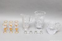 Full lot showing six gold-gilded aperitif glasses, three crystal pitchers, crystal vase, and pair of utensil rests