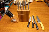 Two knife blocks and multiple knives displayed on a wooden table showing all items in the lot with knives stored and out for display.