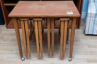 Front view of rectangular stand with four round nesting tables inserted under top, steel ball casters visible on legs