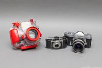 Full lot view of the Olympus underwater housing, Kodak Bantam camera, and Nikkormat camera.