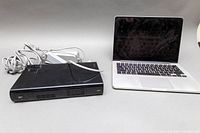 Black Nintendo Wii U console and silver MacBook Pro side by side with AC adapter cable