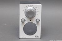 Front view of a silver Tivoli Audio iPAL portable AM/FM radio with tuning and volume controls, speaker grille, and brand markings.