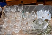 Photo showing multiple crystal wine glasses with etched cut designs arranged upright and some stacked in a cardboard box.