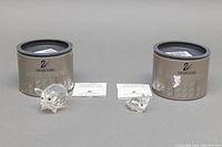 Two Swarovski crystal figurines, pig and bunny, with their original open round boxes and manuals in background.