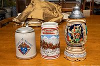 Three beer steins, one Knights of Columbus lidded stein, one Budweiser limited edition stein, and one German musical stein with ornate knight design