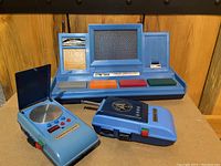 Two blue plastic Star Trek MEGO communicators, one flip-top style with volume/power buttons, one with rectangular shape and Star Trek emblem.