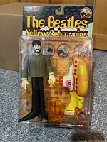 Front view of sealed blister card with George Harrison figure and yellow submarine accessory, showing original packaging and artwork.