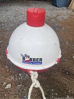 The Big Bobber Floating Cooler sitting on the ground, showing the front logo and attached rope.