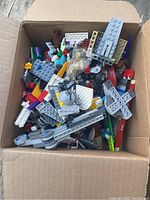 Box filled with mixed LEGO bricks, minifigure parts, and mechanical build elements.
