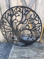 Full view of circular metal tree with birds leaning against wooden fence