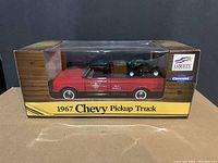 Front view of boxed 1967 Chevy Pickup Truck diecast coin bank showing red truck with black roof inside clear display box.