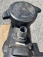Close-up top view of the pump with the circular lid and water inlet fitting visible, showing embossed warning marks.