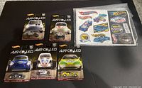 Five Hot Wheels Premium Air Cooled die-cast cars in packaging with a sheet of Hot Wheels Legends Tour collectible stickers on black background.