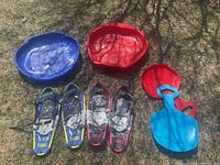 Two pairs of kids snowshoes, two small plastic sleds, one scoop shovel, and one saucer sled on grass surface
