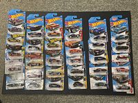 Photo showing 30 new Hot Wheels cars in original blister card packaging laid out in rows, displaying various models and designs.