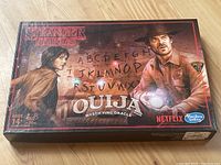 Closed Stranger Things Ouija board game box with character artwork from the series and brand logos.