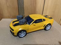 Yellow Bumblebee transformer toy car with dual mounted guns on hood and black racing stripes.