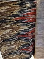 Photo showing the rug with abstract wave pattern in multiple colors including brown, beige, black, orange, and gray tones.