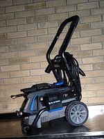 Side view of assembled pressure washer on cart, showing wheels, handle, hose reel, and spray wand attached