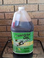 4-liter plastic bottle filled with amber chainsaw oil, label shows green background with chainsaw graphic and brand CHEM-E-CIL