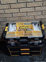 Closed Dewalt tool box with two top organizers stacked on it. Organizers have clear lids showing compartments filled with screws and bolts.