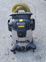 Front view of Dewalt wet and dry vacuum cleaner showing stainless steel body, Dewalt logo, yellow hose coiled on top, black plastic base with wheels.