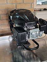 Front side angle of the black 4 stroke 7 HP engine showing pull start, exhaust cover, and metal base frame.