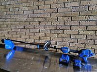 Blue and black cordless Kobalt weed trimmer with rechargeable battery and charger placed on metal surface against brick wall.