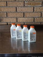 Four white bottles of Stihl Premium two stroke oil with orange caps shown against a brick background.
