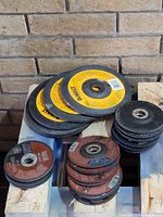 Photo showing various sizes and brands of grinding and cut off disks stacked on a wooden pallet.