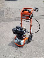 Front angle view showing engine, frame, wheels, hose reel and spray wand