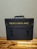 Folded Rocksolar branded black carrying case for foldable solar panel with handle and clip straps