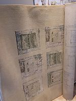 Full view of the beige 5x7 rug rolled partially showing abstract square/rectangle pattern in muted green, gray, and brown tones.