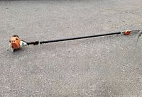 Full side view of Stihl telescopic pole pruner on pavement showing engine housing, shaft, handle and cutting head