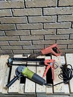 Three tools on pallet: orange manual caulking gun, black and green angle grinder, red electric heat gun.