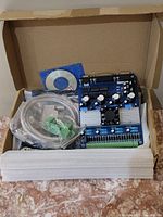 Top-down photo of Ucontrol CNC 3D motion controller board, cables, and software CD inside a cardboard box
