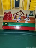 Front of box showing the set displayed with all figurines and stable, festive bow graphic, Peanuts logo and Department 56 branding.